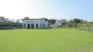A building with a flat roof and a large open grassy area in front. -  The Krati Resort (Bareilly)