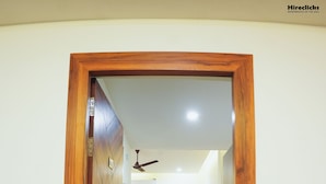 A hallway with a wooden door leading to a room with a bed, a desk, and a mirror. -  The Krati Resort (Bareilly)