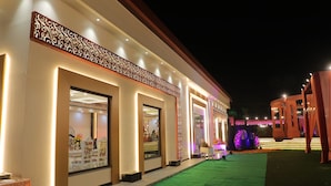 A hotel exterior at night with illuminated entryways, a green carpeted walkway, and decorative lighting. -  The Krati Resort (Bareilly)