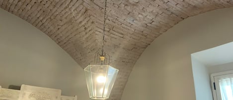 A room with a high, exposed brick ceiling, a hanging lantern-style light fixture, and a white door with a glass panel.