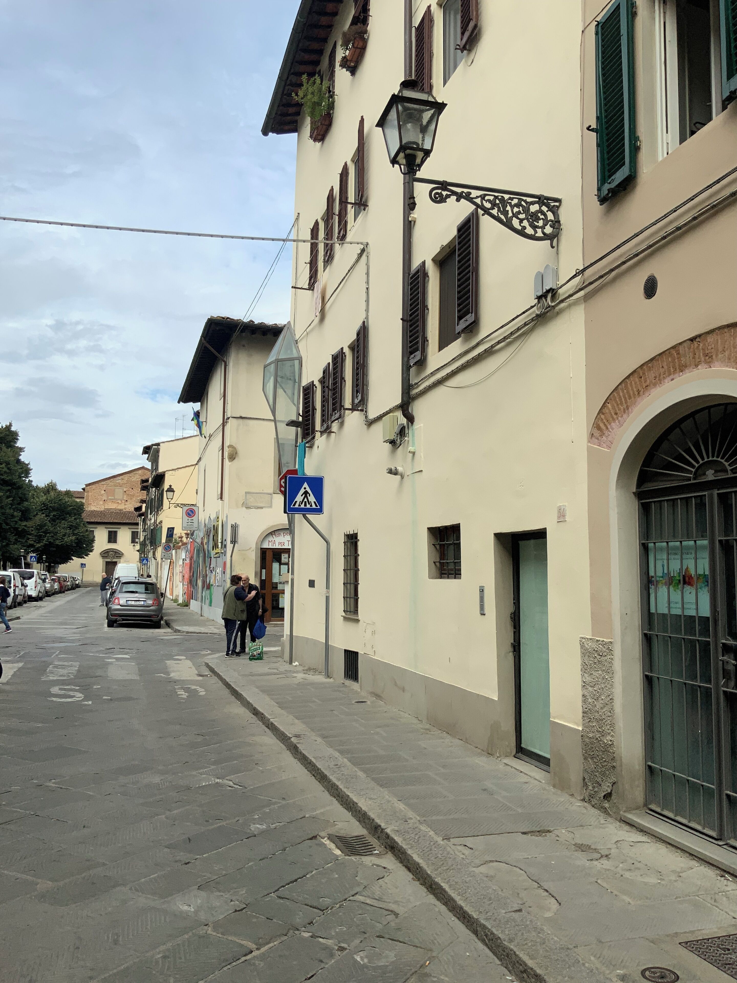 Una strada con edifici, un cartello per l'attraversamento pedonale e un'auto parcheggiata.