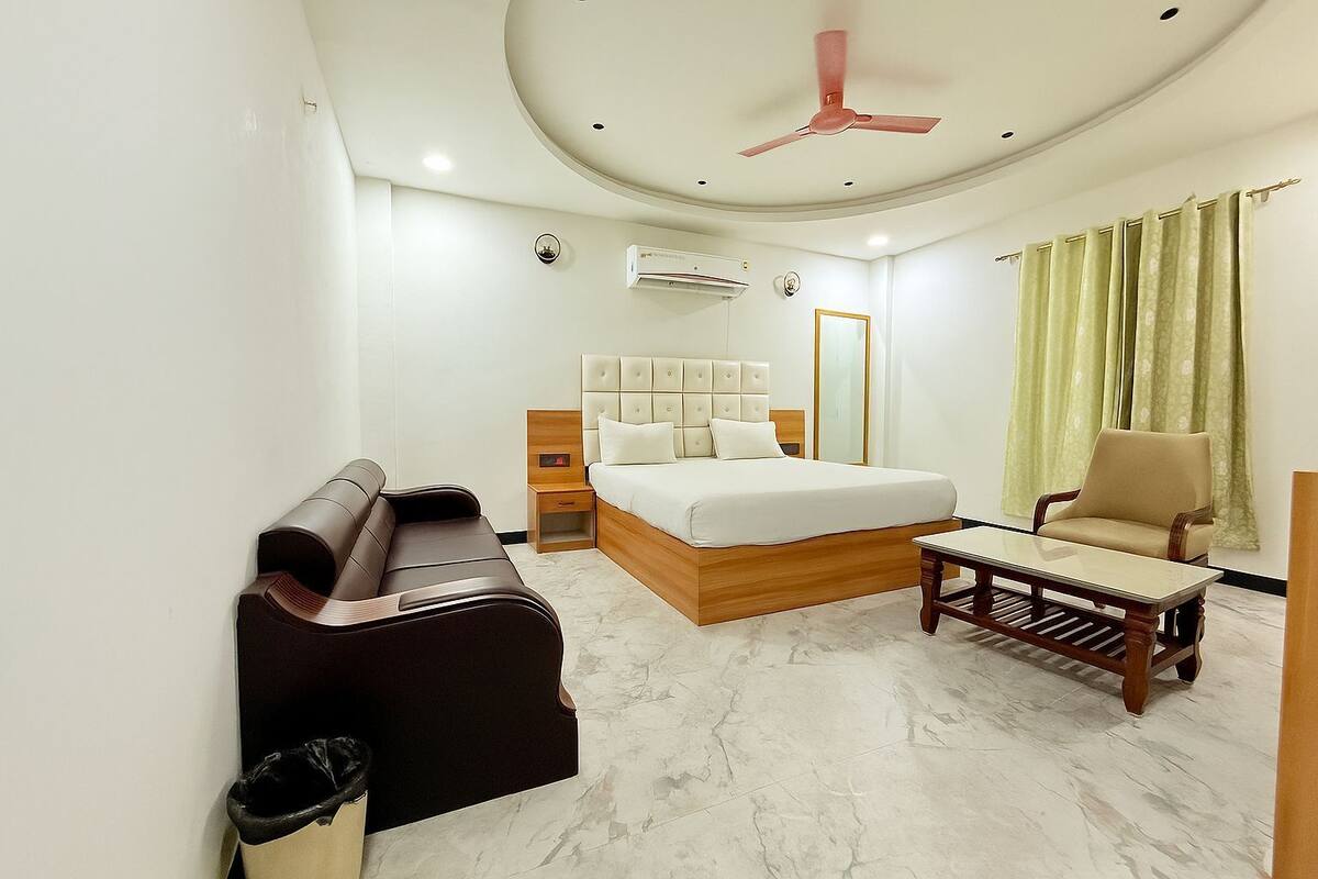 Una habitación de hotel con cama, sofá, sillón, mesita y ventilador de techo.