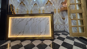 Uma área de recepção com parede de mármore, piso xadrez e porta de madeira com painéis de vidro.