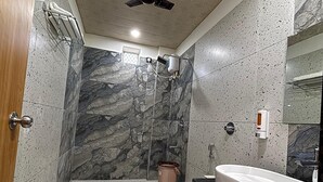 Casa de banho com parede de chuveiro em mármore, banheira independente, lavatório moderno e ventoinha no teto.