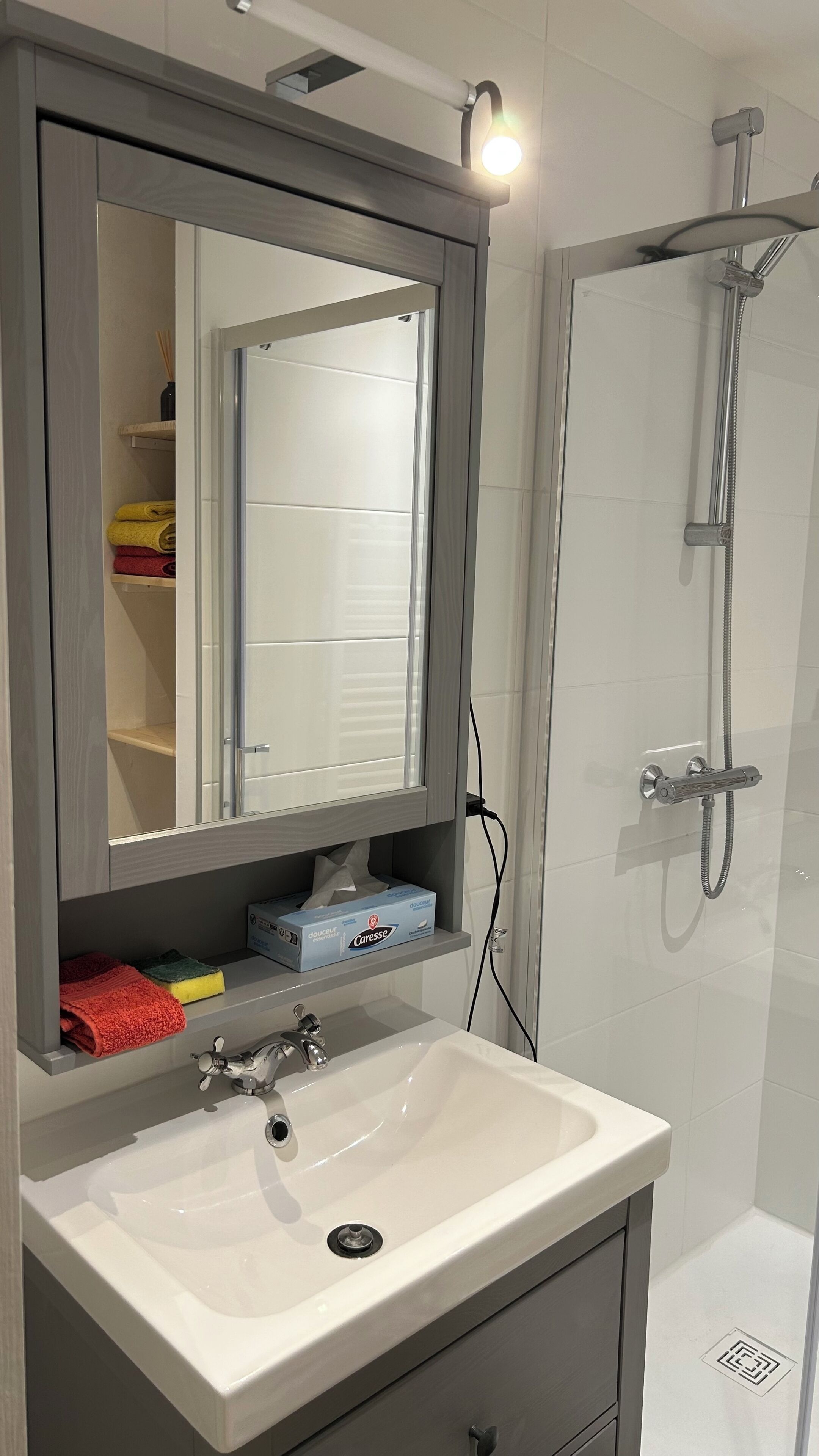 A bathroom with a white sink, a mirror, a shower, and a towel rack with folded towels.