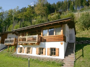 Eine zweistöckige Chalet mit Holzbalkonen, einer Steintreppe und Blick auf einen bewaldeten Hang.