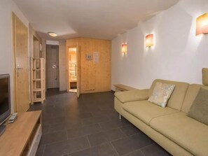 A living room with a sofa, a TV, a wooden door, and a shower area.