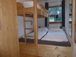 A bunk bed room with a wooden ladder, a window with curtains, and a view of the outside.