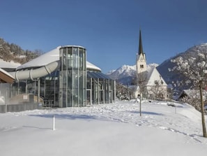 A modern building with a glass facade and a traditional church with a steeple in a snowy landscape.