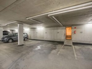A parking garage with concrete floors, columns, and walls, featuring numbered parking spaces and a fire extinguisher.