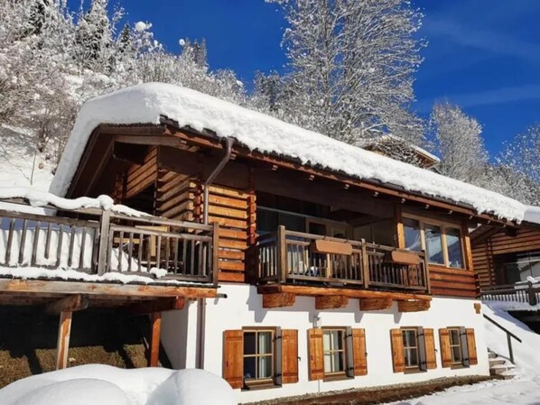 A wooden chalet with a balcony, surrounded by snow-covered trees.