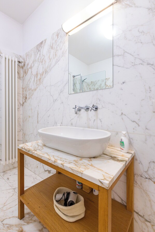 A bathroom with a marble sink, wooden vanity, and a mirror. - DESIGN APARTMENT IN THE HISTORIC CENTER OF MILAN (Milano)