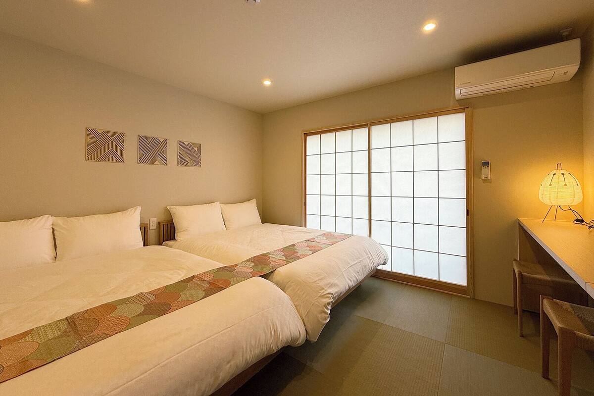 Een hotelkamer met twee bedden, een groot raam met uitzicht en een bureau met een lamp.