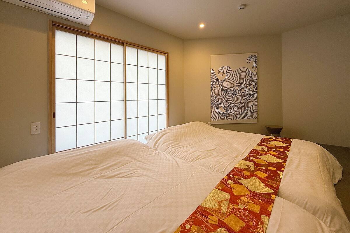 Een hotelkamer met een groot bed, een schuifdeur van shoji-hout, een aan de muur bevestigd kunstwerk en een aan het plafond gemonteerde airconditioner.