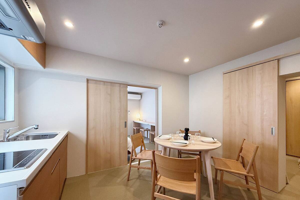 Een moderne keuken met een spoelbak, fornuis en kasten, een eethoek met een ronde tafel en vier stoelen, en een houten deur.