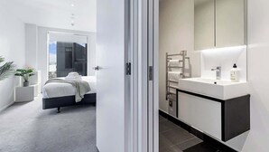 Una camera da letto moderna con un letto, un comodino e un grande specchio sopra il lavabo.