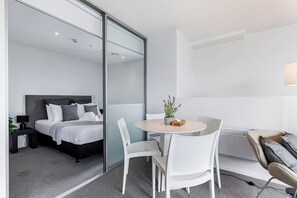 A modern hotel room with a bed, a round table with chairs, a small potted plant, and a sofa.