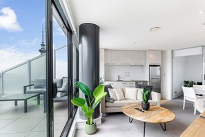 A modern apartment with a balcony, a living area with a sofa and coffee table, a kitchen, and a dining area. - Pool, Gym & Modern 2BR Sky Tower View by Zodiak (Auckland)