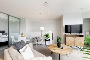 A modern hotel room with a sofa, a dining table, a TV, and a cabinet. - Pool, Gym & Modern 2BR Sky Tower View by Zodiak (Auckland)