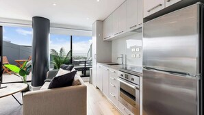 Una cucina moderna con elettrodomestici in acciaio inossidabile, una zona pranzo con divano e tavolo, e un balcone con piante e vista.