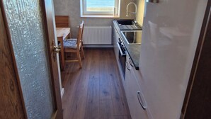 A compact kitchen with a window overlooking the sea, a radiator, and a wooden chair. - Apartment 54m² for 1-4 persons directly on the dike, sea view from kitchen and living room (Dahme)