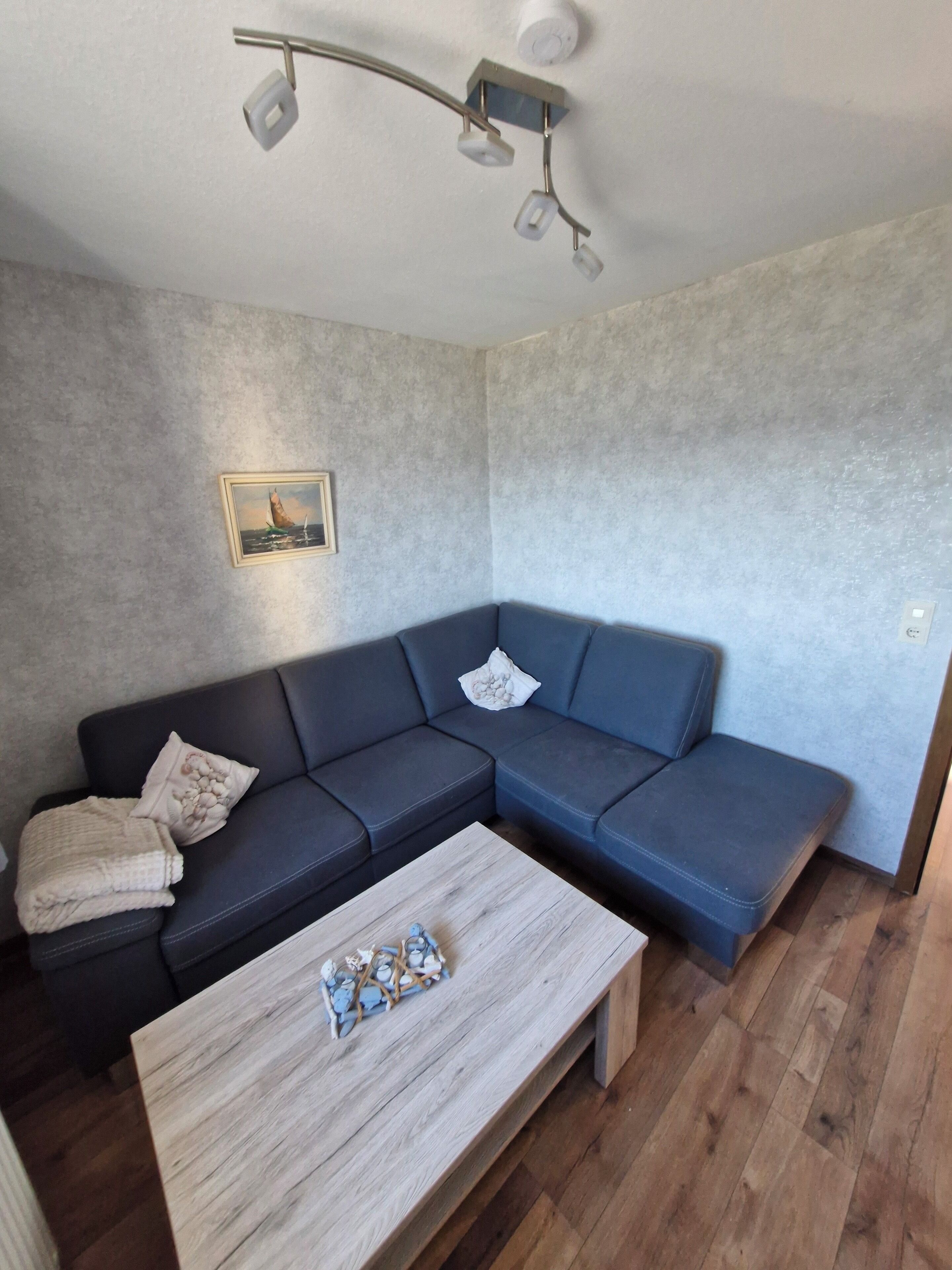A modern living room with a sectional sofa, a wooden coffee table, and a wall-mounted light fixture.