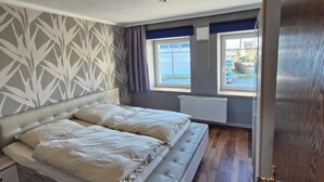 A bedroom with a large bed, a window with a view, and a radiator. - Apartment 54m² for 1-4 persons directly on the dike, sea view from kitchen and living room (Dahme)