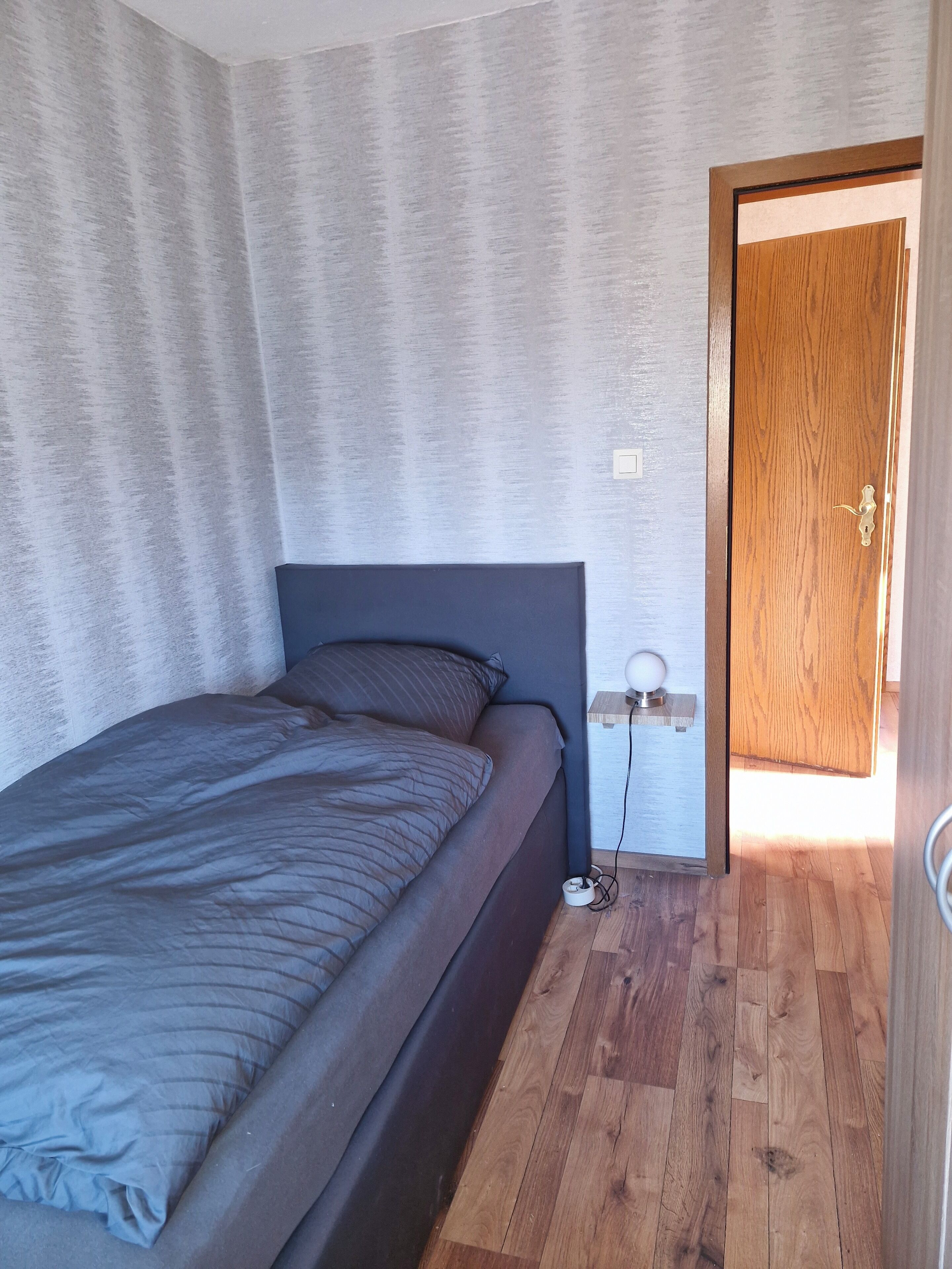 Un dormitorio con cama, mesita de noche, puerta de madera y pared con textura.