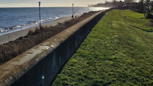 Une promenade en bord de mer, dotée d’une barrière en béton, de zones herbeuses et offrant une vue sur la mer.