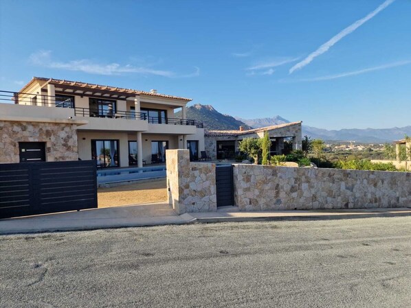 A modern two-story house with a stone facade, a balcony, and a view of mountains in the background. - VILLA WITH OCEAN AND MOUNTAIN VIEWS (PALASCA)