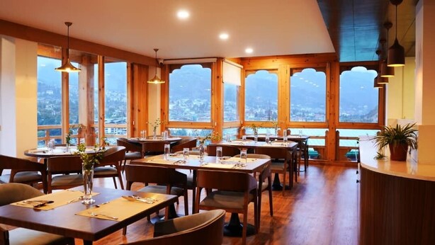 A restaurant with wooden interior and large windows offering a city view. - Tro Hotel (Thimphu)