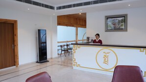 A reception area with a wooden reception desk, two chairs, a large framed picture on the wall, and a wooden door. - Tro Hotel (Thimphu)