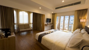 A hotel room with a large bed, a sofa, a desk with a coffee maker, a TV, and a view of the city through large windows. - Tro Hotel (Thimphu)