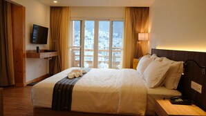 A hotel room with a bed, a TV mounted on the wall, a bedside table with a phone, and a window with a city view. - Tro Hotel (Thimphu)