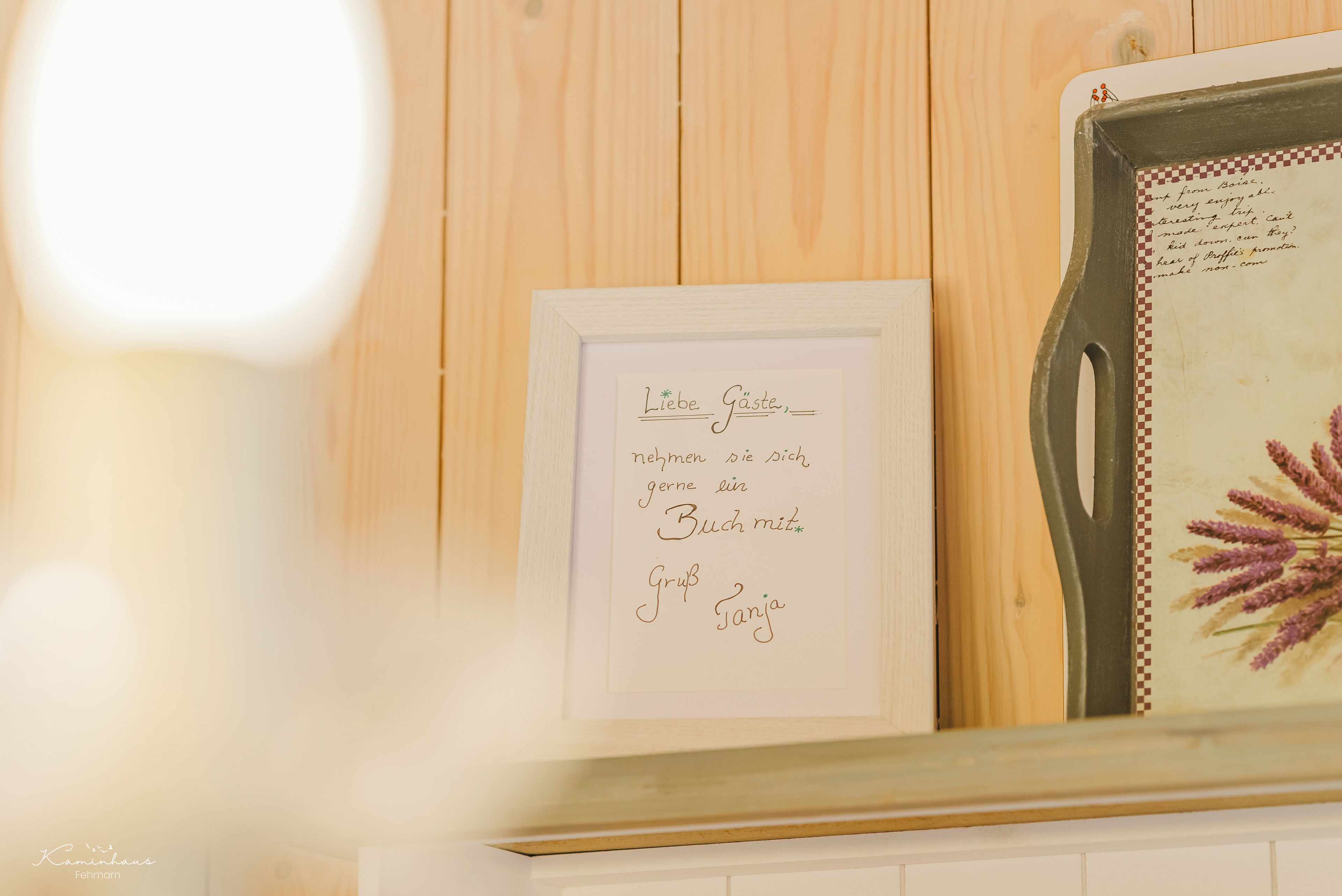 A framed sign with text in a foreign language, a decorative tray with a floral design, and a wooden wall background.