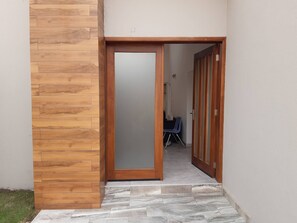Une porte en bois donne sur une pièce où se trouvent une chaise bleue et une petite table.
