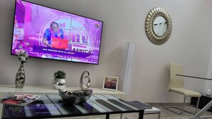 Un salon moderne avec un téléviseur à écran plat, une table basse en verre, un canapé, un fauteuil et un miroir décoratif.