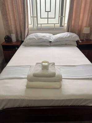 A neatly made bed with white linens, a folded towel, and a candle on the bed. - Serene Oasis in East Legon Hills - Chic 2 Bedroom Retreat (Santeo)