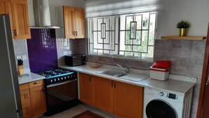 Une cuisine compacte dotée de meubles en bois, d’une cuisinière à gaz, d’un four à micro-ondes, d’un évier et d’un lave-linge encastré.