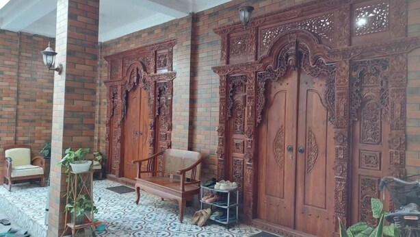Espacio interior con puertas de madera ornamentadas, una silla, un estante pequeño con zapatos y un felpudo.