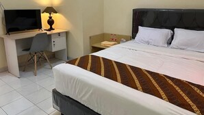 Habitación de hotel con cama, escritorio con computadora, silla y mesita de noche con lámpara.