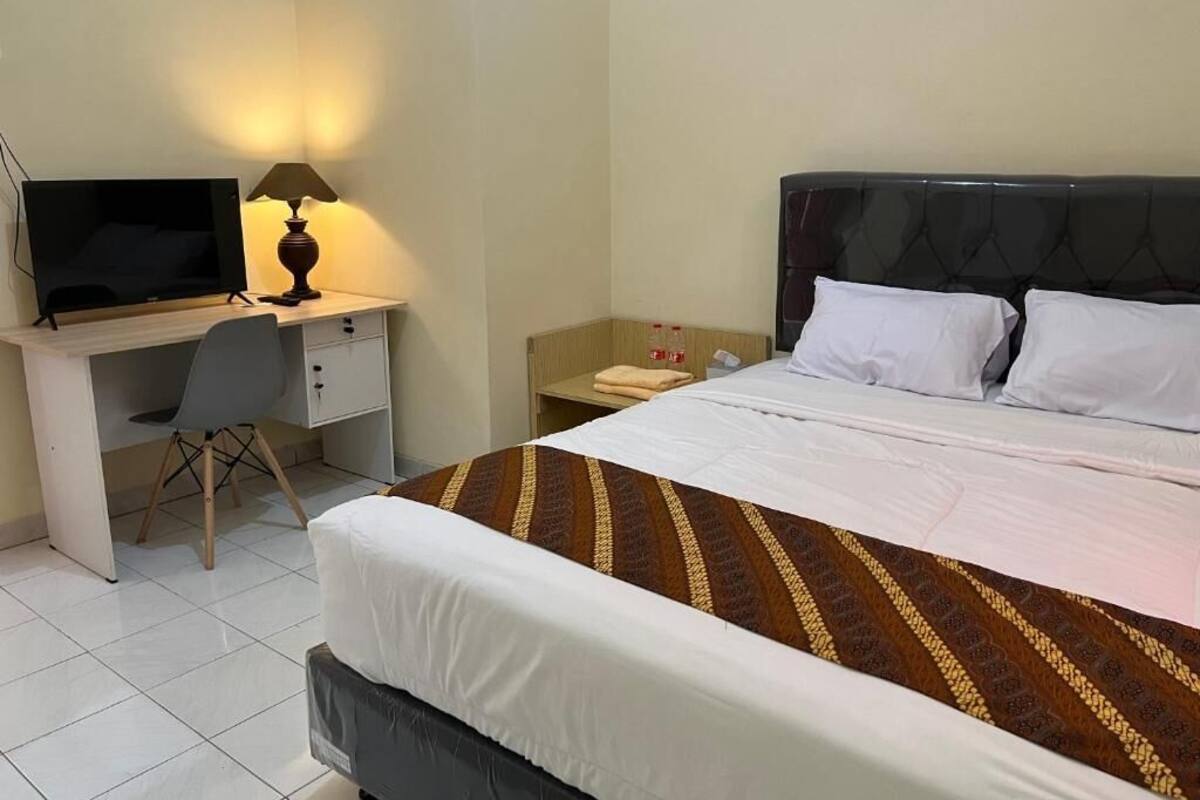 Une chambre d’hôtel comprenant un lit, un bureau avec un ordinateur, une chaise et une table de chevet avec une lampe.