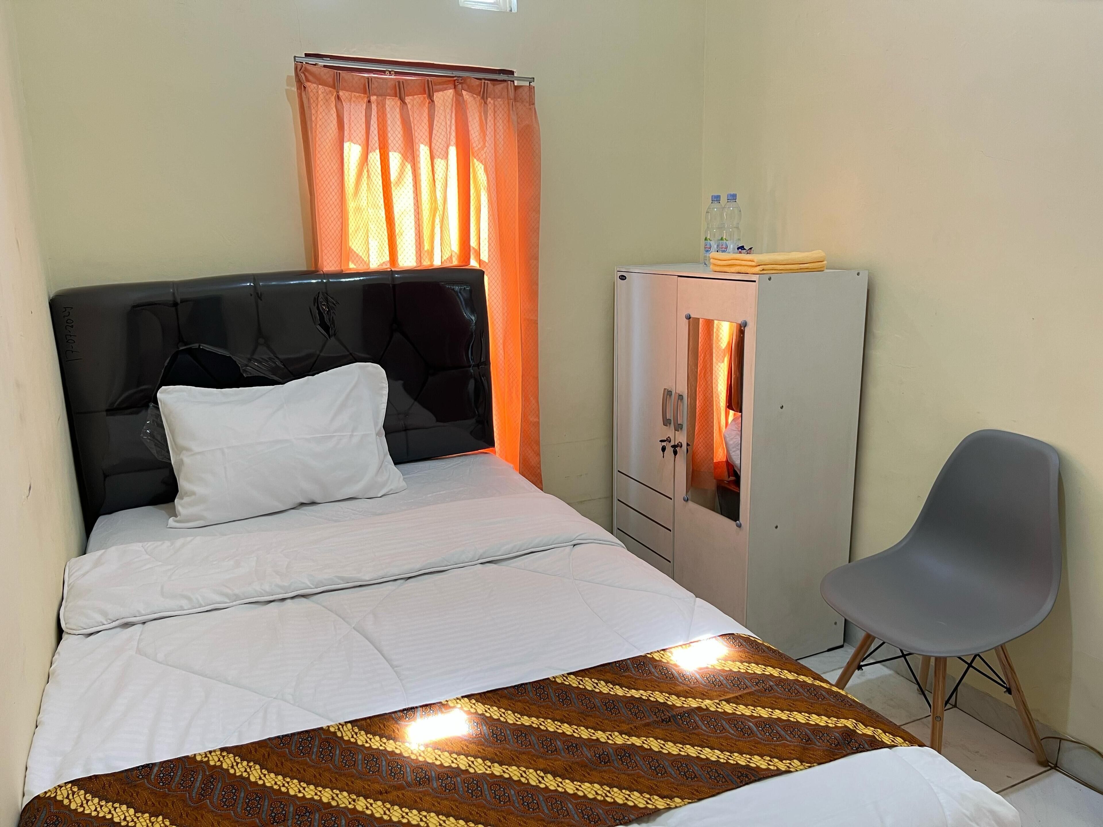 Una cama bien hecha con un almohadón blanco, una silla gris y un armario con espejo.