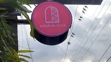 A circular sign with a geometric pattern and the text "ndalem tirt" against a cloudy sky.