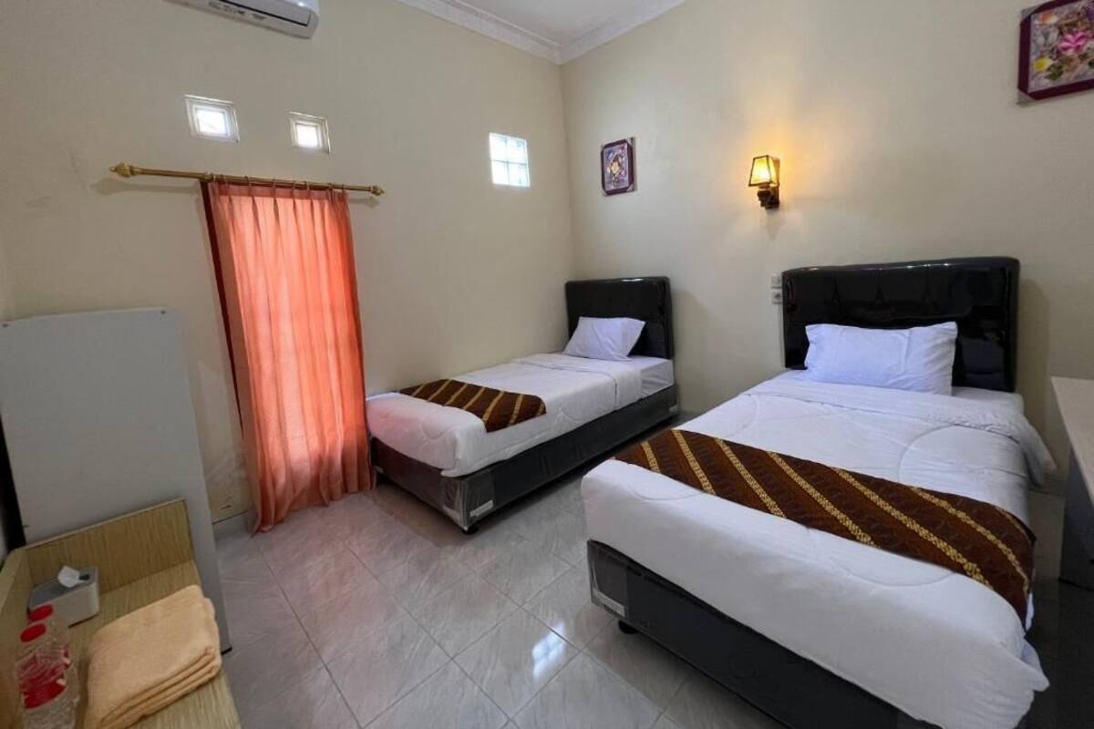 Une chambre d’hôtel avec deux lits, une petite table avec une chaise, un climatiseur et une fenêtre avec un rideau.