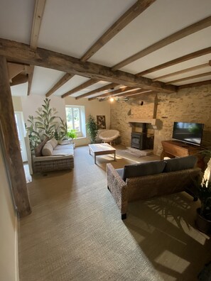 Een gezellige woonkamer met een stenen open haard, een televisie en een comfortabele zithoek met een bank en fauteuils.