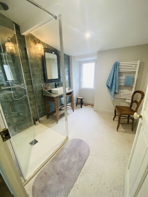 Un baño con ducha de mampara de vidrio, tocador con espejo y ventana que proporciona luz natural.