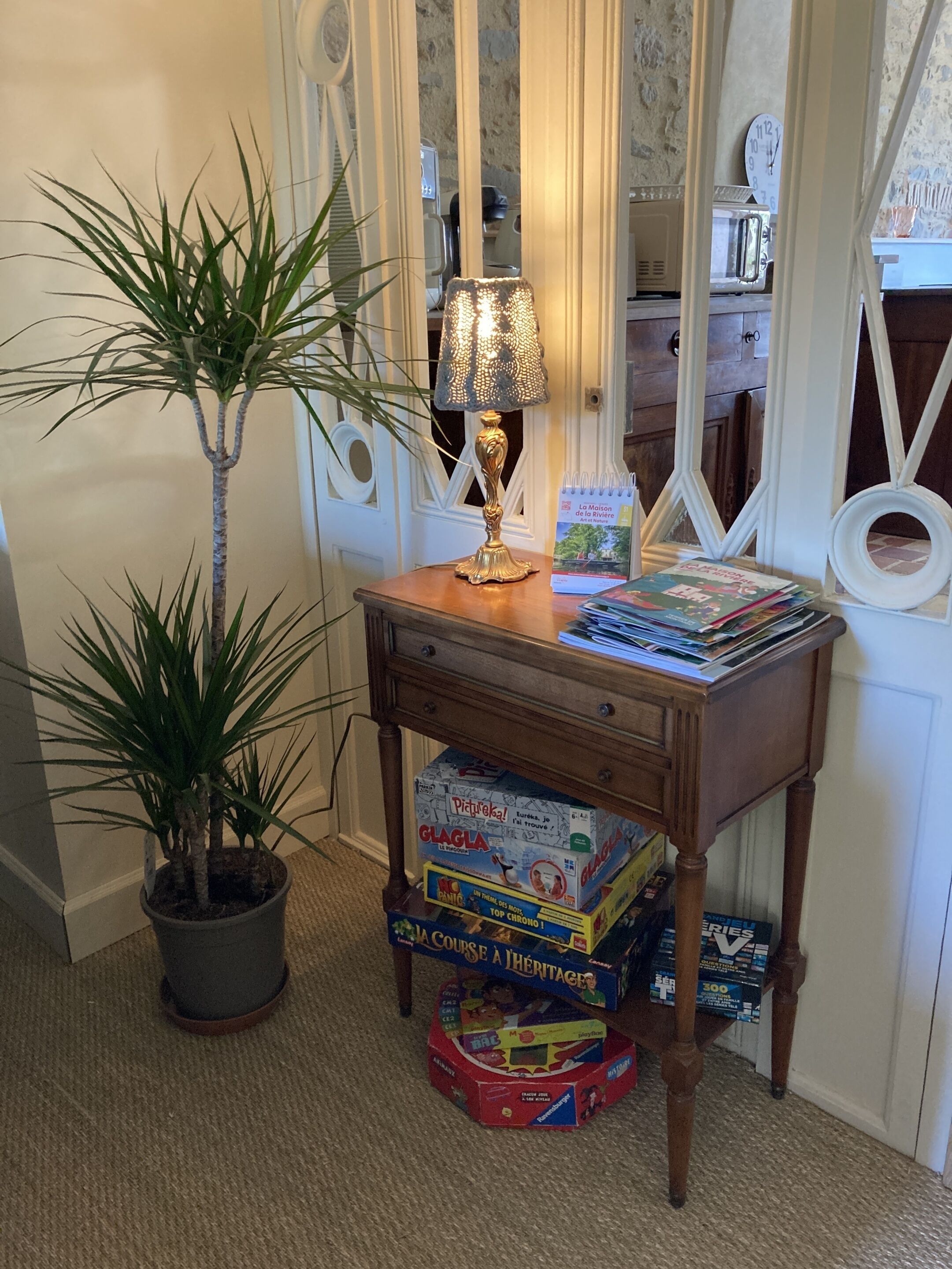 A corner with a wooden side table holding a lamp, a potted plant, and several board games.