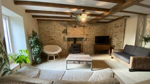 Un salon chaleureux avec un mur en pierre, une cheminée, un canapé, un téléviseur et une table basse en osier.