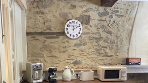 Une cuisine avec un mur en pierre, une horloge, une machine à café, une bouilloire, un grille-pain et un four à micro-ondes.